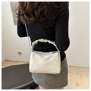 Detail of white marble textured handbag featuring pleated handle and gold chain strap