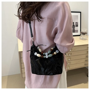 Detail of a black bucket bag with marble texture and colorful beads strap