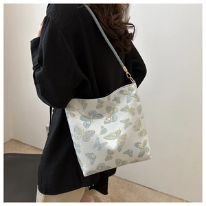 Detail of embroidered butterfly patterns on beige shoulder bag with blue strap