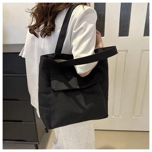 Sac fourre-tout minimaliste en toile noire avec poche avant porté à l'épaule par un mannequin