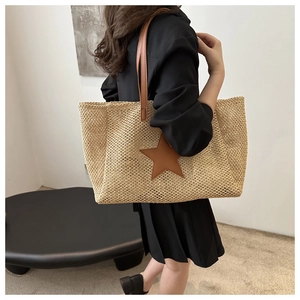 Detail view of woven straw tote bag featuring a brown star and leather shoulder straps
