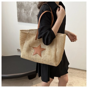 Detail of a large woven straw tote bag with brown leather star accent and handles