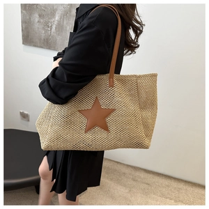 Detail of woven straw shoulder bag featuring a brown star patch and leather strap