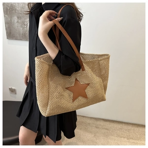 Detail of woven straw tote bag with brown leather star patch and handles worn by model