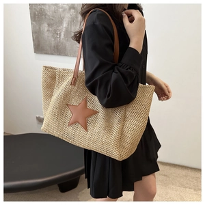 Detail of woven straw tote bag featuring a large brown leather star and shoulder straps