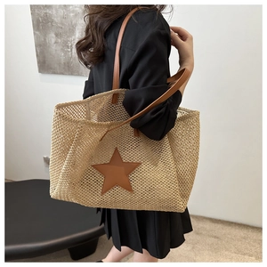 Detail of woven straw tote bag featuring brown leather star appliqué and slim shoulder strap