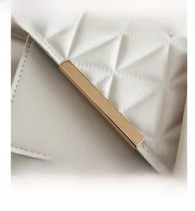Macro detail of creamy white quilted leather texture with gold metal bar on the handbag flap