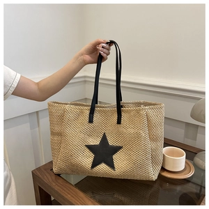 Close-up of woven straw tote bag featuring a large black star patch and slim handles