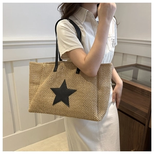 Detail of woven straw shoulder bag featuring a prominent black star patch and slim strap