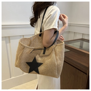 Detail of hand-woven straw tote bag with black star patch and leather shoulder strap