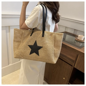 Detail of hand-woven straw tote bag with black leather star patch and long shoulder strap