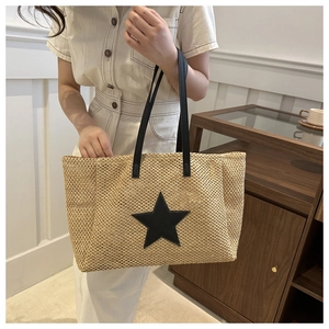 Close-up of woven straw tote bag with black leather star patch and durable handles