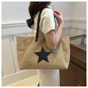 Detail of woven straw tote bag featuring a black leather star patch and long shoulder strap