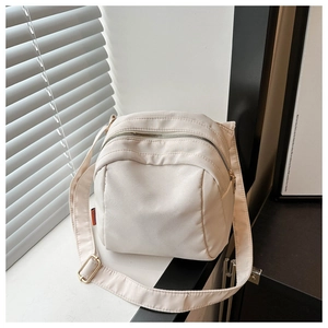Détail d'un sac bandoulière en toile crème avec fermeture éclair et étiquette orange