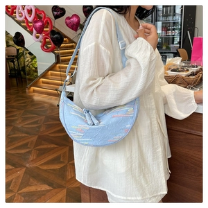 Close-up of light blue crescent bag with monogram embossing and colored embroidery