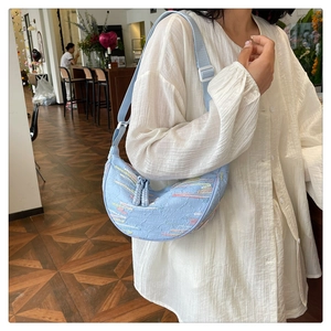 Close-up of a light blue striped crossbody bag with embroidery on a female model