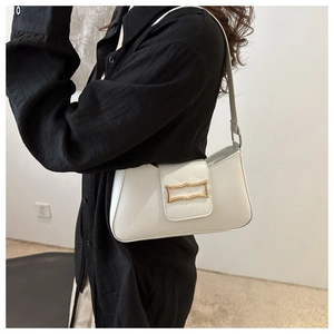 Detail view of a creamy white underarm bag with a golden metal buckle worn over the shoulder
