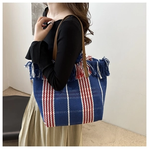 Detail of colorful striped canvas tote with fringe trim and leather handles on model
