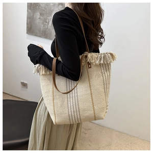 Detail of woven tote bag with fringe edge and leather straps on model in minimal setting