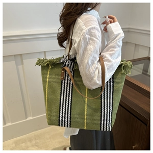 Shoulder shot of large green woven tote bag with fringe details and striped pattern