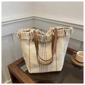 Detail of bohemian striped woven tote bag featuring long fringes and brown leather handles