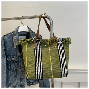 Detail of green straw tote bag featuring vertical stripes, tassels and brown leather handles