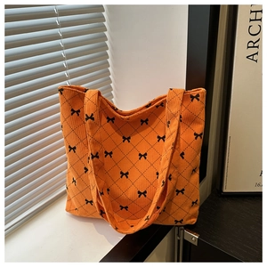 Dettaglio borsa tote in velluto a coste arancione con fiocchi neri e motivi a rombi