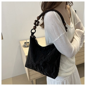 Detail of black tote bag with unique wood bead handle and textured pleated fabric