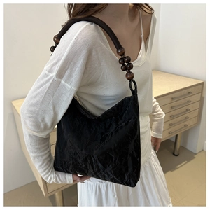 Detail of black tote bag featuring distinctive crinkled texture and wooden bead strap