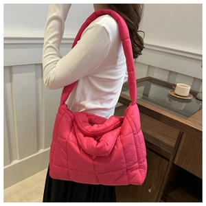 Detail view of pink quilted puffer tote bag worn by a model in a modern indoor setting