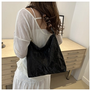 Detail of black pleated tote bag featuring large dark wood bead shoulder strap accents