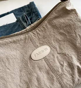 Κοντινό πλάνο μπεζ τσάντας με σούρες, σήμα FASHION και λεπτομέρειες υφής από νάιλον