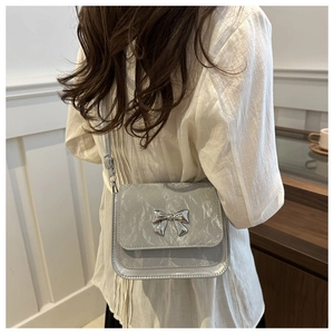 Detail of silver crossbody bag featuring metallic bow and marble texture on model