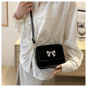 Detail of black crossbody square bag with elegant silver bow ornament and leather texture