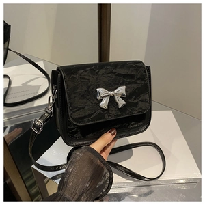 Detail of black square shoulder bag featuring pleated texture and silver metal bow buckle