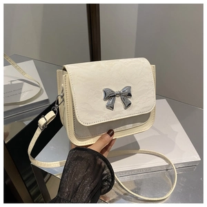 Detailed macro view of cream square crossbody bag with textured leather and silver bow