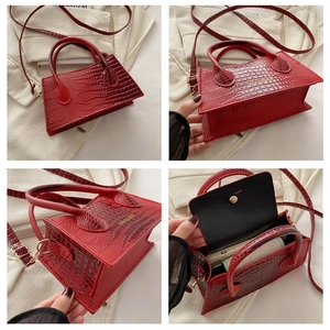 Detail van rode tas met krokodillenpatroon, gouden hardware en trapeziumstructuur