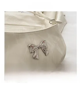 Close-up of cream shoulder bag with shiny pleated texture and silver metal bow detail