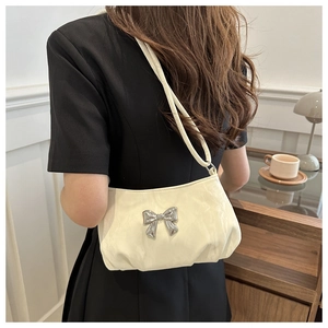 Close-up of cream crossbody bag featuring a silver bow and textured leather pleats
