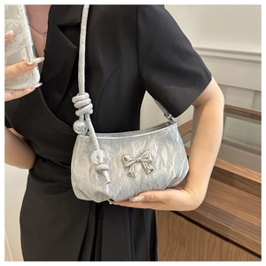 Close-up of silver pleated crossbody bag with metal bow detail and woven rope strap