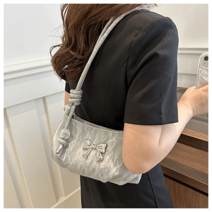 Detail of silver metallic shoulder bag featuring a metal bow and beaded knotted strap