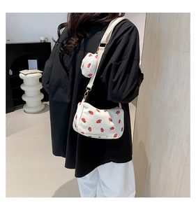 Detail of white corduroy crossbody bag featuring red strawberry prints and a round coin purse