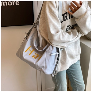 Detail van lichtblauwe nylon tas met geel Ha borduursel en brede schouderband