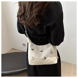 Détail d'un sac à bandoulière blanc orné de papillons 3D noirs et argentés