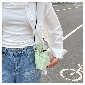 Light green nylon drawstring mini bag shown in a casual outdoor crossbody lifestyle shot
