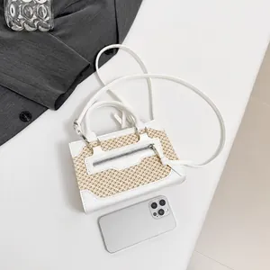 Miniature crossbody bag with leather trim next to a smartphone for size reference