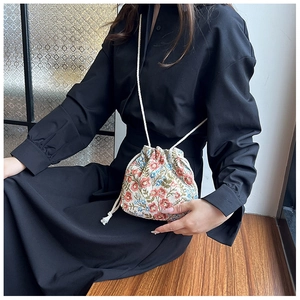 Detail of floral bucket bag with drawstring and white braided strap worn by a model