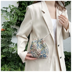 Floral embroidery detail on a mini drawstring bucket bag with woven shoulder strap