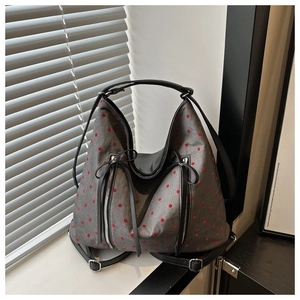 Detail der grauen Canvas-Tasche mit roten Punkten, schwarzen Trägern und Silberbeschlägen