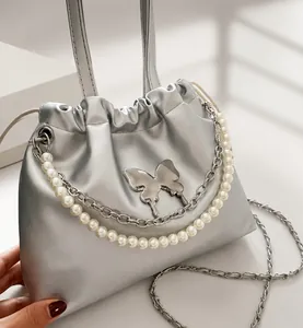 Détail d'un sac seau argenté métallisé avec pièce papillon en métal et chaîne de perles